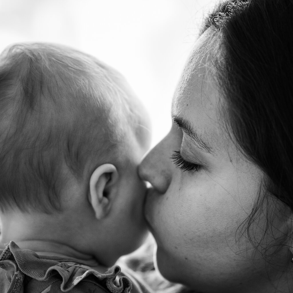 Novorozeneck&eacute; focen&iacute; - maminka jemně l&iacute;b&aacute; sv&eacute; miminko, černob&iacute;l&aacute; fotografie.