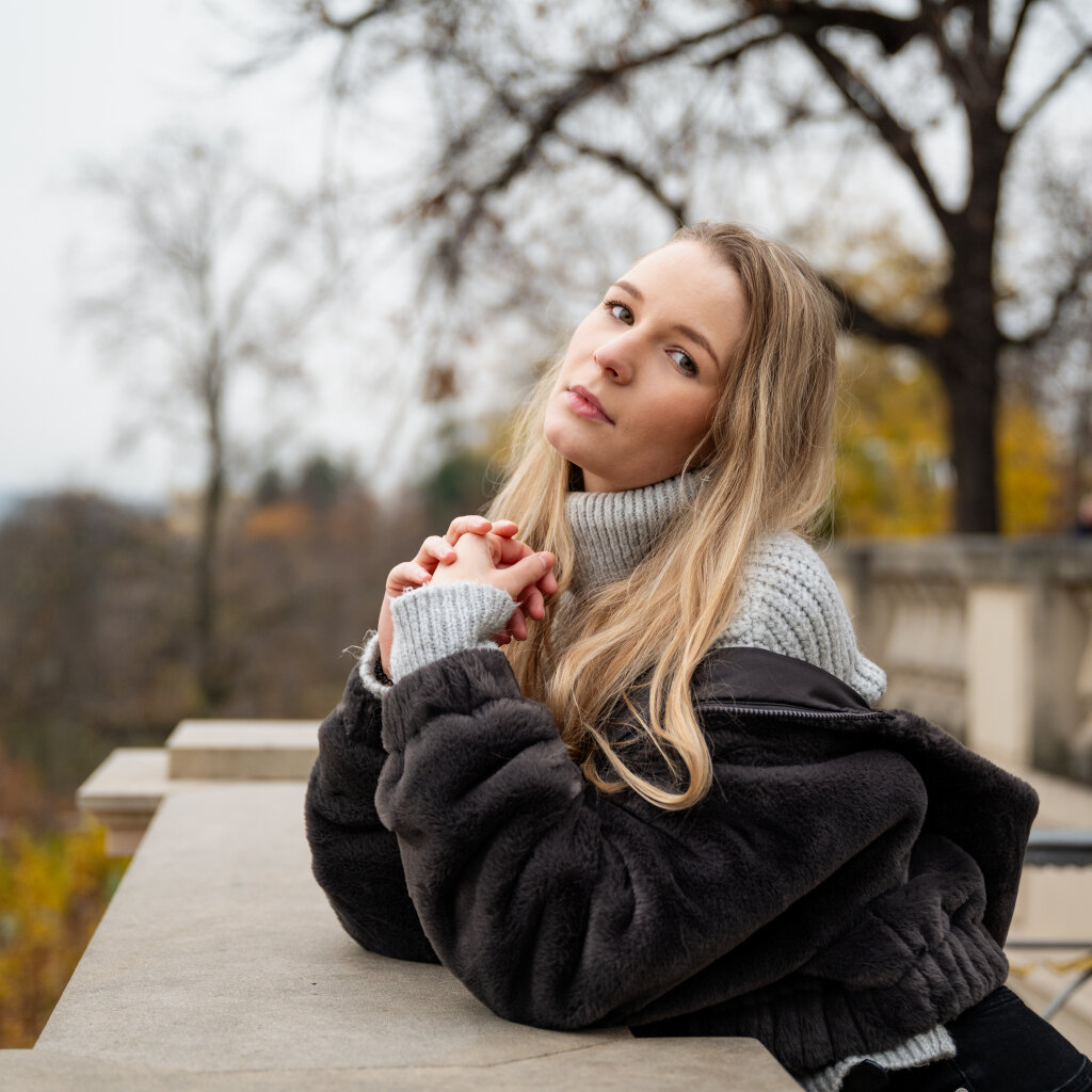 Portr&eacute;t zamy&scaron;len&eacute; blond&yacute;ny v pleten&eacute;m svetru opřen&eacute; o z&aacute;bradl&iacute; v podzimn&iacute;m parku.