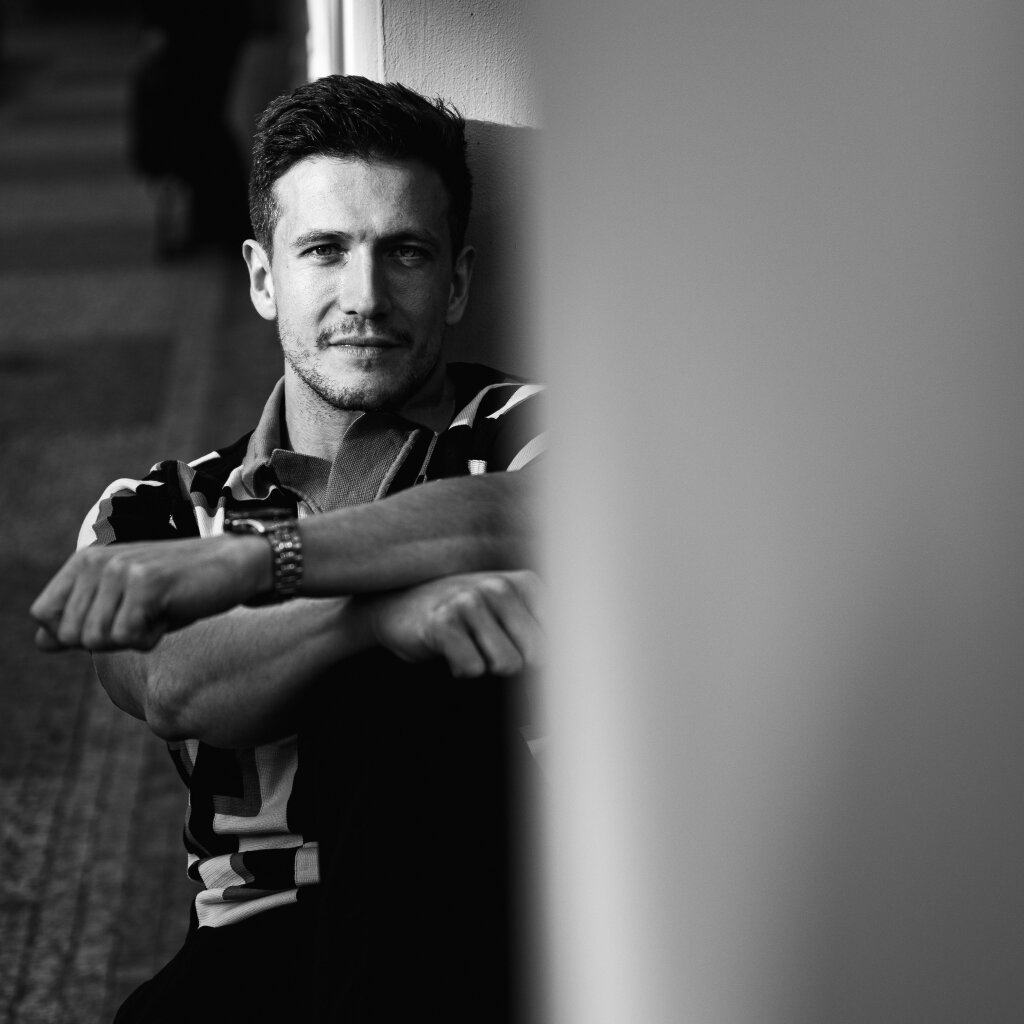 Černob&iacute;l&aacute; portr&eacute;tn&iacute; fotografie muže s rukama zkř&iacute;žen&yacute;ma na kolenou.