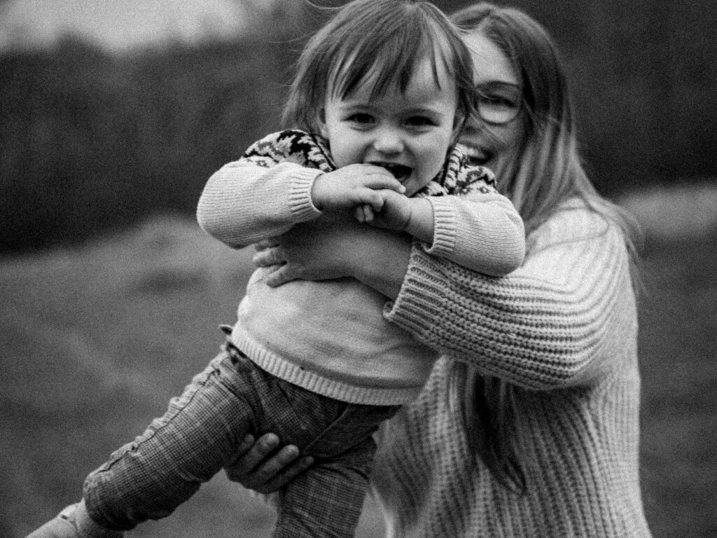 Maminka se toč&iacute; s rozesm&aacute;t&yacute;m batoletem v n&aacute;ruč&iacute; &ndash; černob&iacute;l&aacute; fotografie.