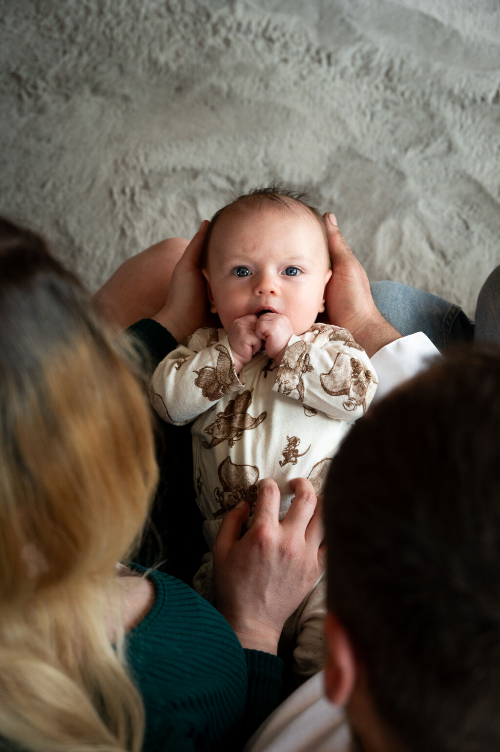 Rodinn&eacute; focen&iacute; - miminko s modr&yacute;ma očima lež&iacute; na nohou rodičů a ti se nad n&iacute;m skl&aacute;něj&iacute;.