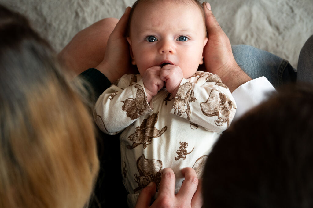 Rodinn&eacute; focen&iacute; - miminko s modr&yacute;ma očima lež&iacute; na nohou rodičů a ti se nad n&iacute;m skl&aacute;něj&iacute;.