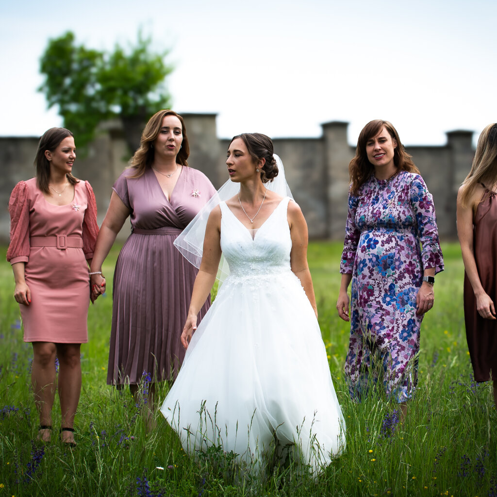 Nevěsta kr&aacute;č&iacute; s družičkami po rozkvetl&eacute; louce.