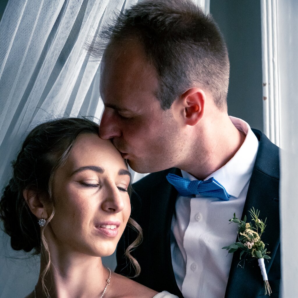 Ženich l&iacute;b&aacute; nevěstu na čelo u okna - intimn&iacute; svatebn&iacute; moment.