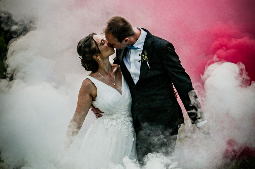 Polibek novomanželů obklopen&yacute;ch barevn&yacute;m růžov&yacute;m a b&iacute;l&yacute;m d&yacute;mem na louce.