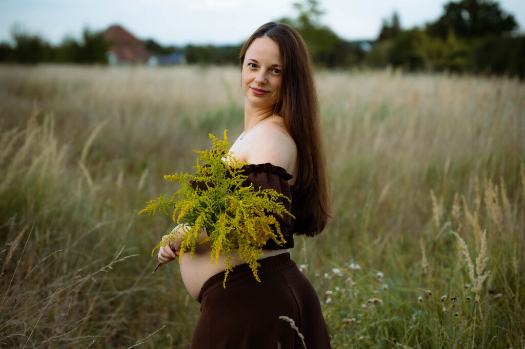Těhotn&aacute; maminka v hněd&eacute; sukni s kytic&iacute; zlatob&yacute;lu na letn&iacute; louce.