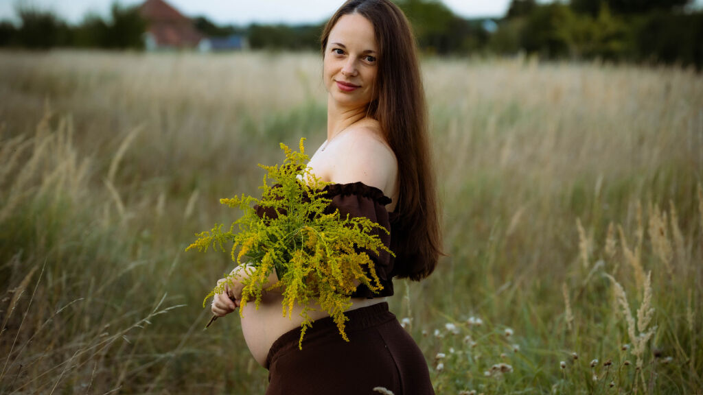 Těhotn&aacute; maminka v hněd&eacute; sukni s kytic&iacute; zlatob&yacute;lu na letn&iacute; louce.