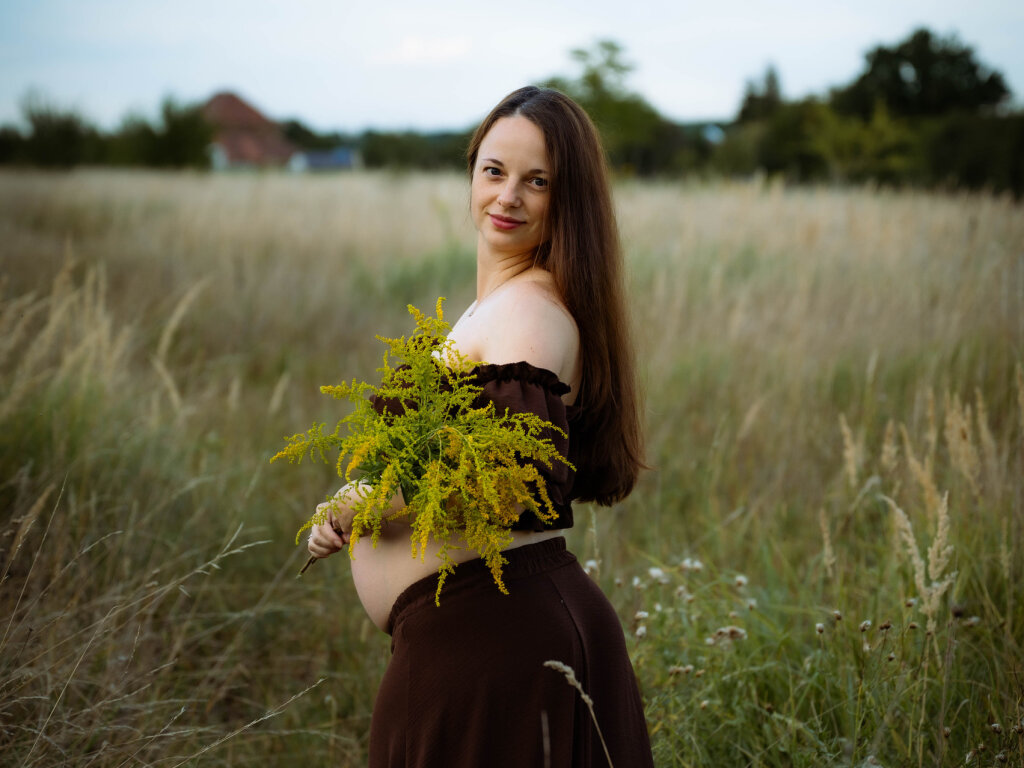 Těhotn&aacute; maminka v hněd&eacute; sukni s kytic&iacute; zlatob&yacute;lu na letn&iacute; louce.