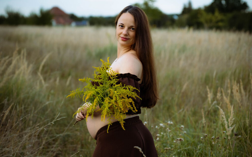 Těhotn&aacute; maminka v hněd&eacute; sukni s kytic&iacute; zlatob&yacute;lu na letn&iacute; louce.
