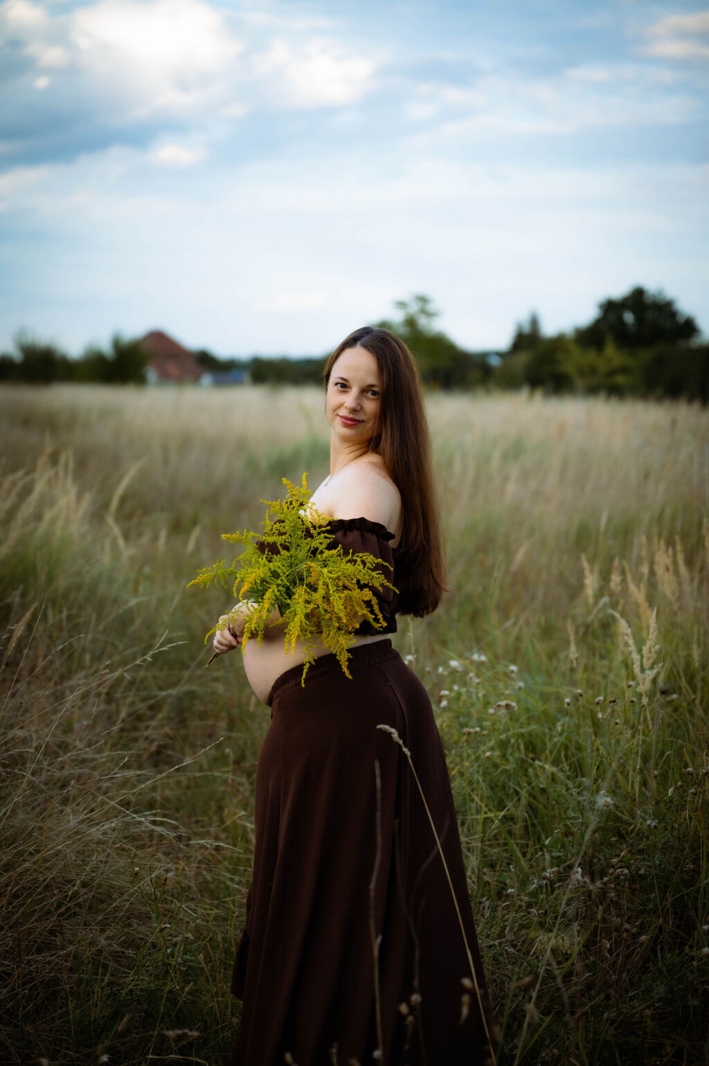Těhotn&aacute; maminka v hněd&eacute; sukni s kytic&iacute; zlatob&yacute;lu na letn&iacute; louce.