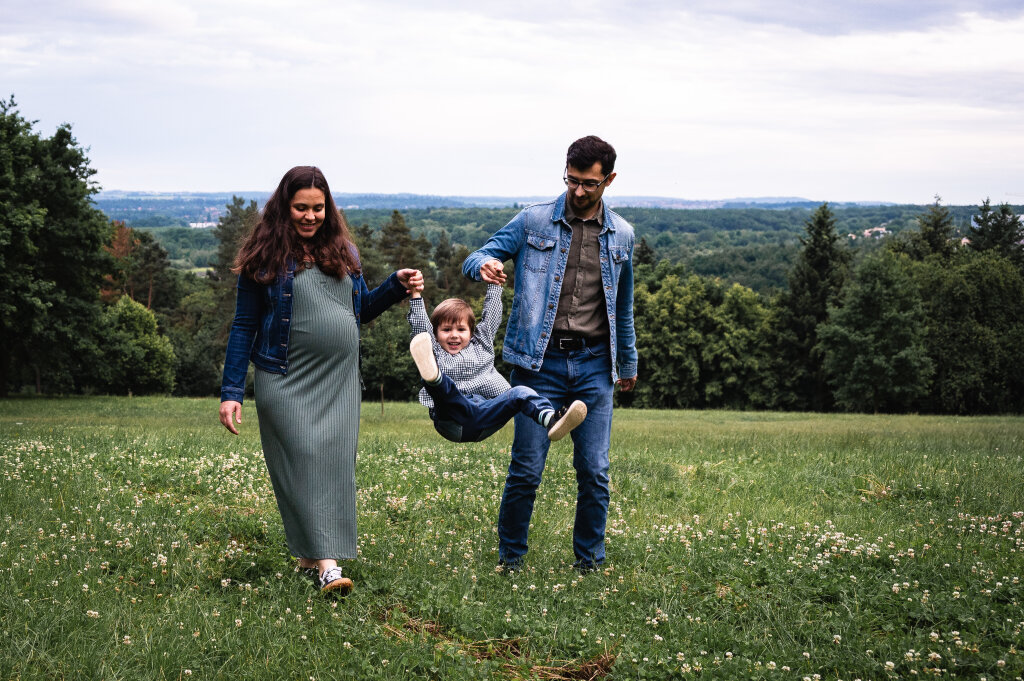 Těhotn&aacute; maminka s tat&iacute;nkem houpou synka za ruce na zelen&eacute; louce.